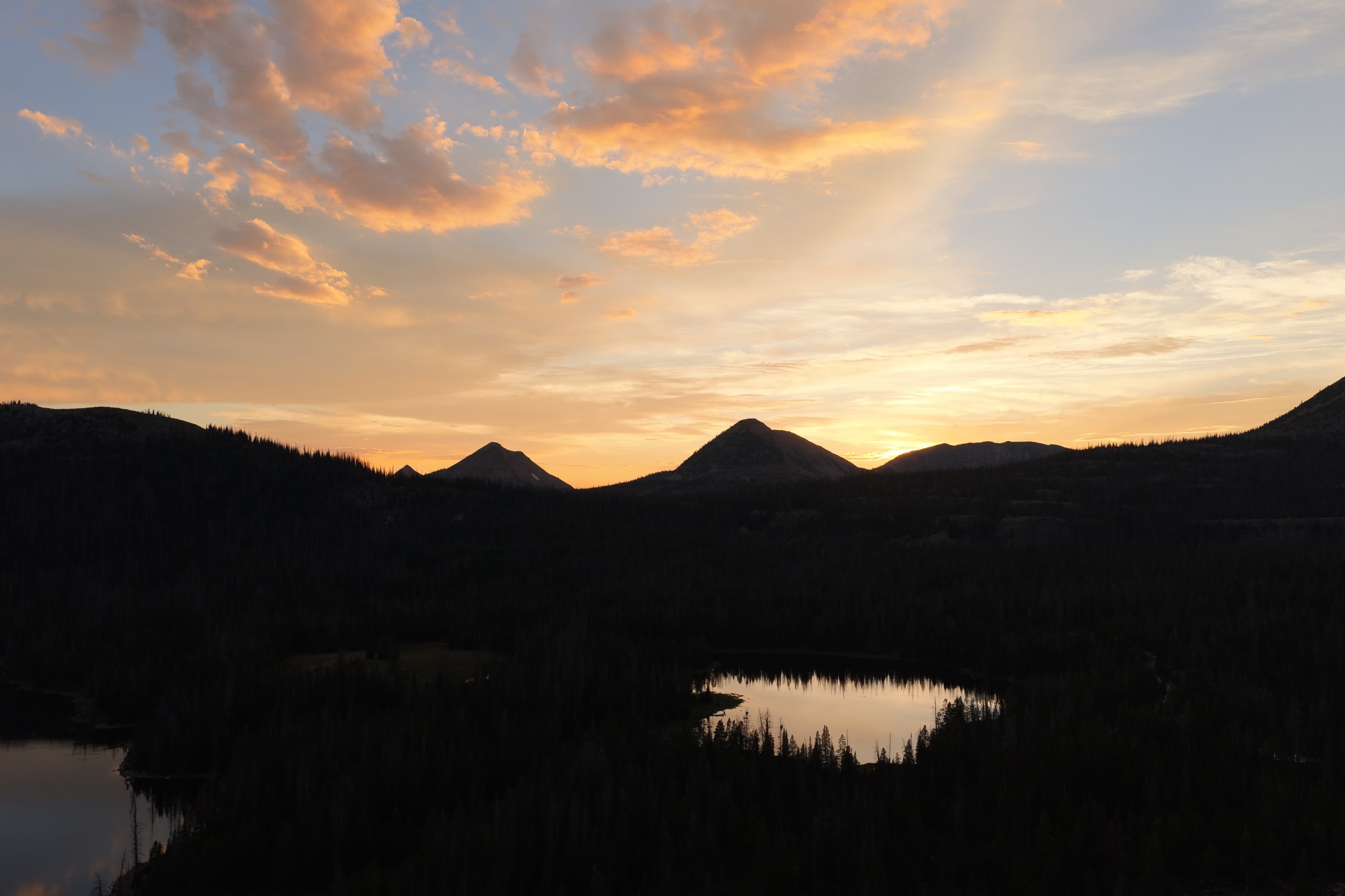 Golden sunset clouds above forested mountains and reflecting alpine lakes.